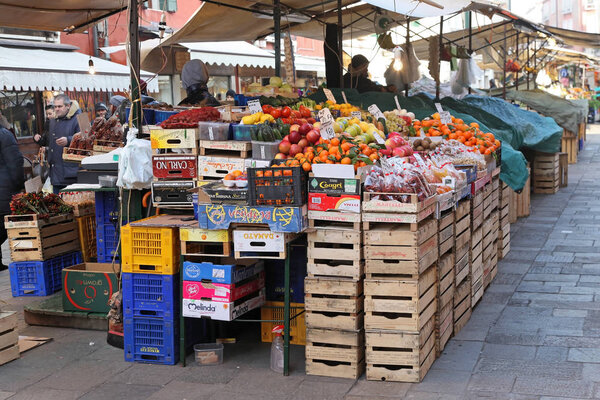 VENICE, ITALY - DECEMBER 18, 2012: Busy food market famous Mercato di Rialto in Venice with lots of people buying fresh organic fruits and vegetables from market stalls.