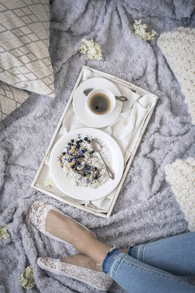 female legs on bed and breakfast with coffee on white tray, top view 