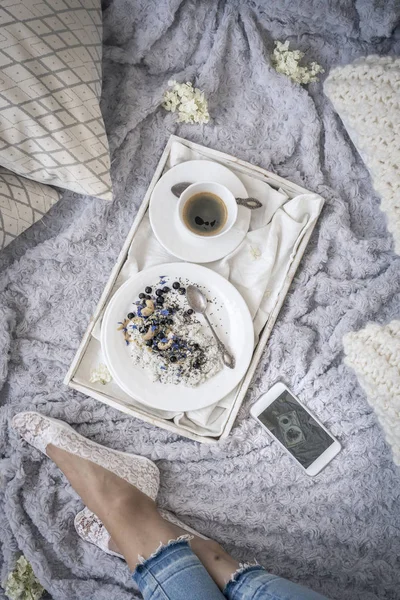 female legs on bed and breakfast with coffee on white tray, top view
