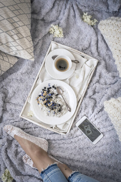 female legs on bed and breakfast with coffee on white tray, top view 