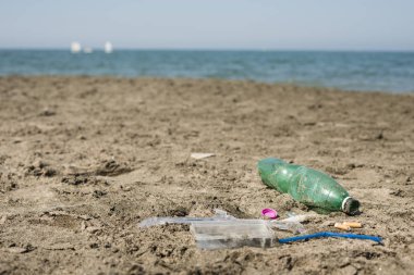 Yeşil, plastik şişe, pamuk temizleme bezi, kap, kutu ve sigara kumlu bir plaj üzerinde yaptı.