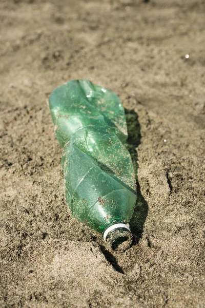 Green, plastic bottle left on a sandy beach.