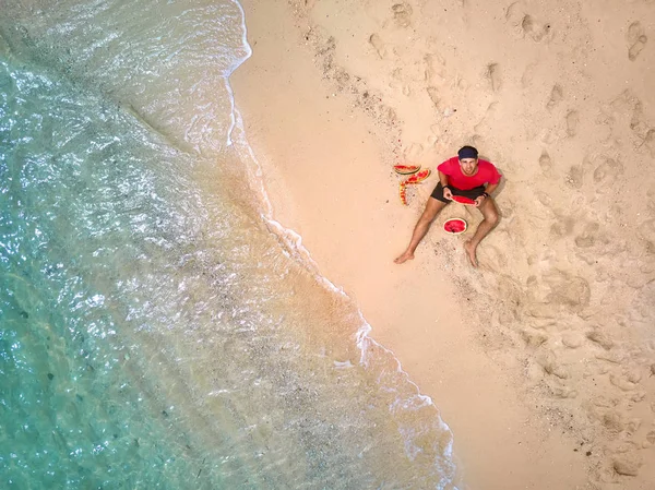 Barefoot man is het eten van watermeloen op zand strand — Stockfoto