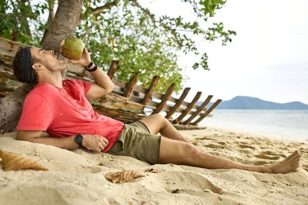 Mann mit Stoppeln trinkt am Sandstrand aus Kokosnuss — Stockfoto