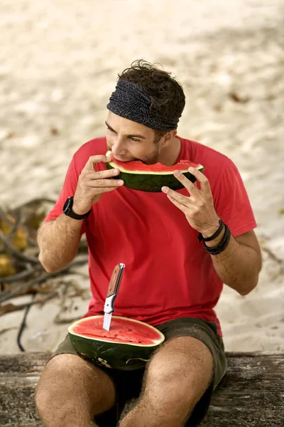 Man with stubble is eating watermelon on sand beach — Stock Photo, Image