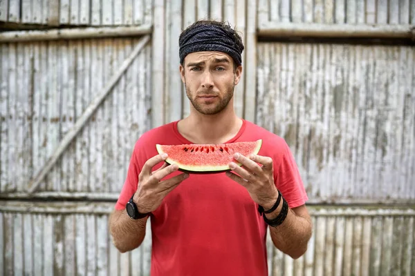 Man with stubble holds slice of watermelon on wooden fence background