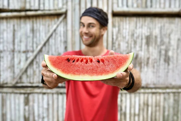 Lächelnder Mann mit Stoppeln hält Scheibe Wassermelone auf Holzzaun Hintergrund — Stockfoto