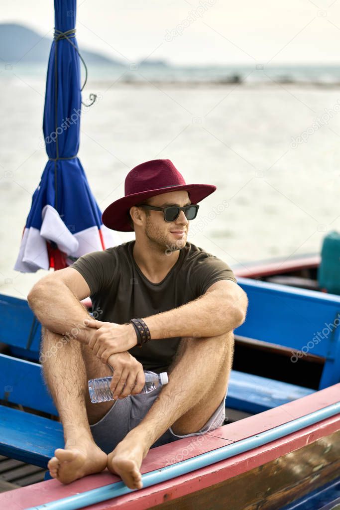 Tanned man with stubble is sailing on colorful boat