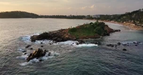 在海岸线的背景和斯里兰卡梅里萨多云的天空中 人们都在这里的岩石绿色岛屿上 海浪正在海浪压在它的岸边 具有向前运动的空中录像 — 图库视频影像