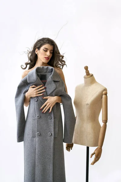 Modelo cobre seu corpo com casaco cinza perto do manequim de costura — Fotografia de Stock