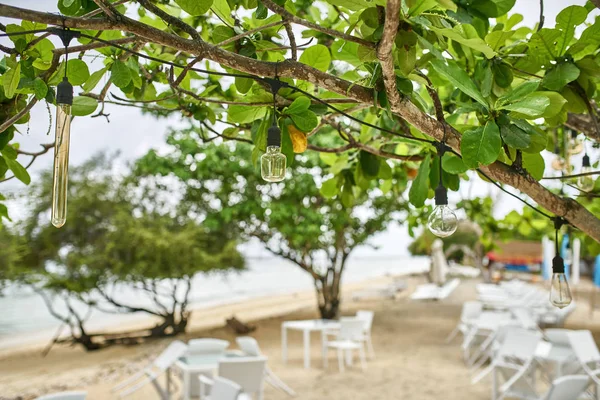 Tropischer Sandstrand mit Café im Freien mit weißen Möbeln und hängenden Edisonlampen — Stockfoto