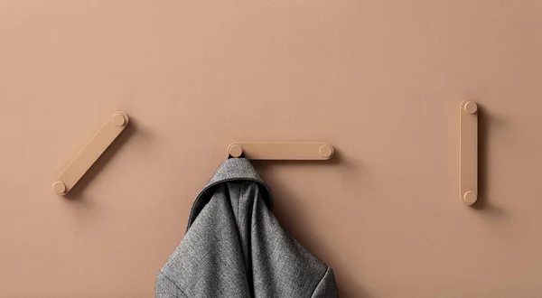 Fancy coral metal hangers with hanging gray jacket on colorful wall in studio — Stock Photo, Image