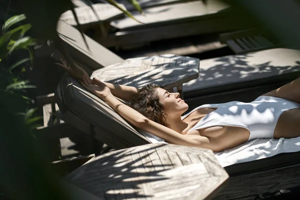 Bruna ragazza in costume da bagno prendere il sole sulla sedia a sdraio in legno — Foto Stock