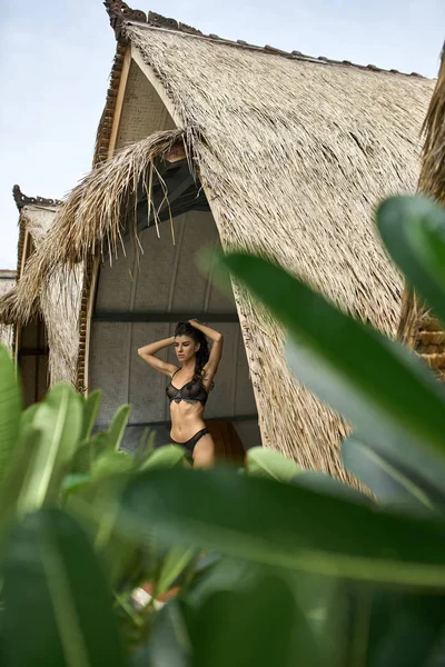 Mujer morena en lencería oscura sexy posando en bungalow en un resort tropical — Foto de Stock