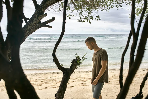 Chico guapo se para en la playa de arena tropical — Foto de Stock