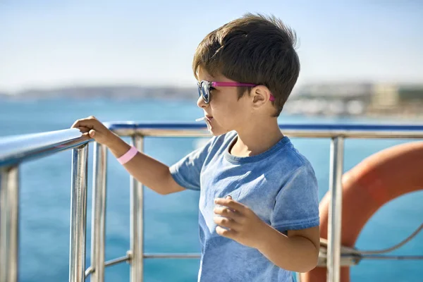 Small boy in sunglasses eating lollipop on yacht deck — Stock Photo, Image