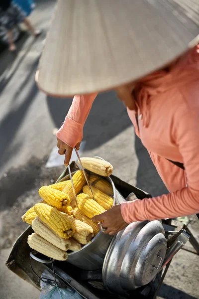 Asiático vendedor em chapéu cônico tradicional venda de milho cozido — Fotografia de Stock