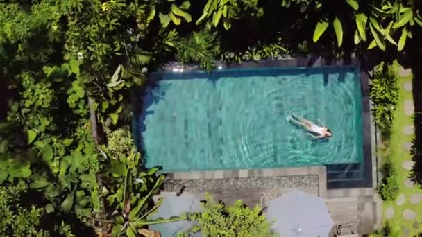 Brunette girl is swimming in outdoor pool on villa between tropical plants — Stock Video