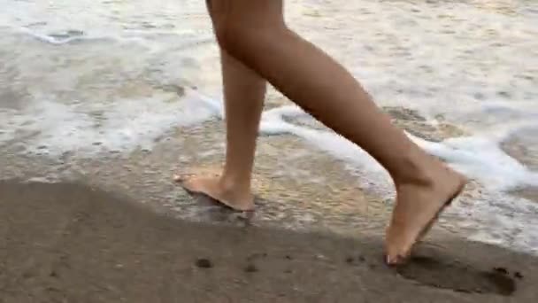 Ragazza abbronzata che cammina sulla spiaggia sullo sfondo ondulato del mare — Video Stock