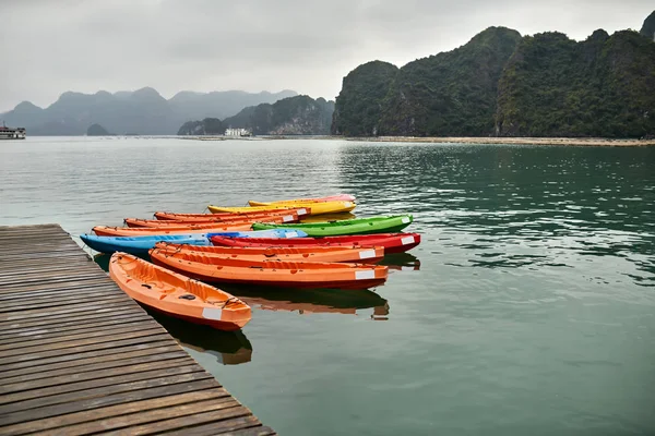 Multicolored canoes moored to wooden pier on nature background — Stock Photo, Image