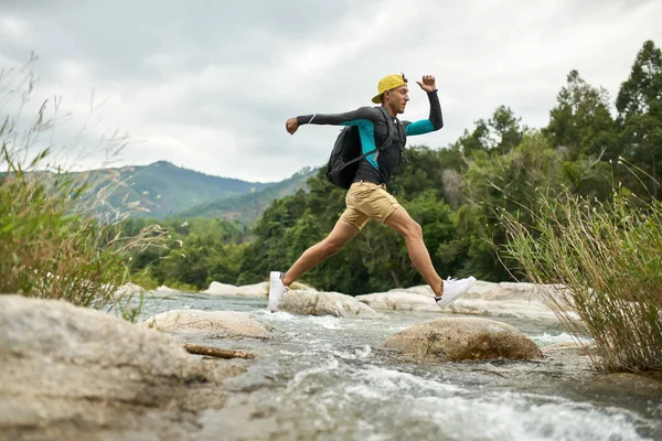 Traveler running through shallow rocky river on nature background — Stock Photo, Image