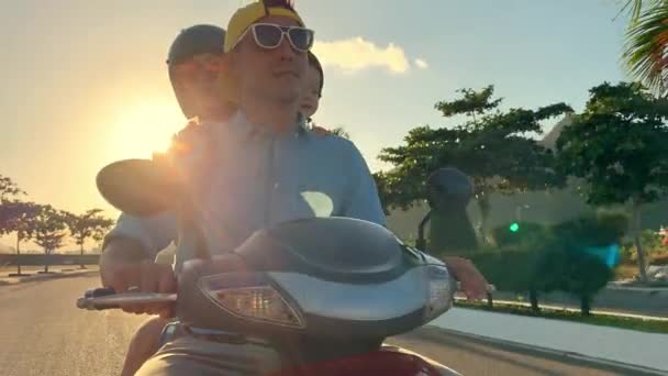 Родители со своим маленьким ребенком едут на мотоцикле по солнечной улице города — стоковое видео