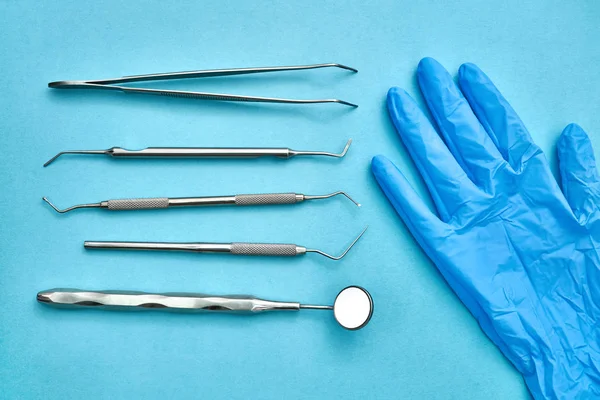 Dental instruments and protective glove lying on blue surface — Stock Photo, Image