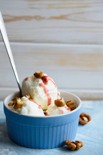 Delicious white ice cream with nuts and fruit syrup on a blue background