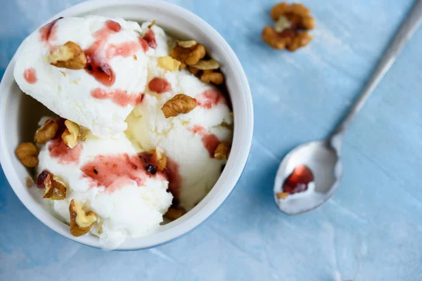 Delicious white ice cream with nuts and fruit syrup on a blue background