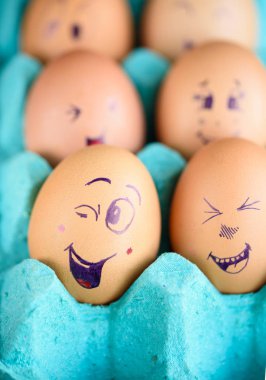 Neşeli çörek üzerinde mavi bir tavada yumurta. Yumurta farklı yüzleri. Duygular.