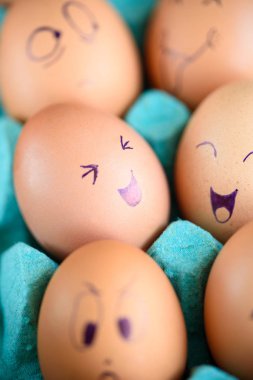 Neşeli çörek üzerinde mavi bir tavada yumurta. Yumurta farklı yüzleri. Duygular.