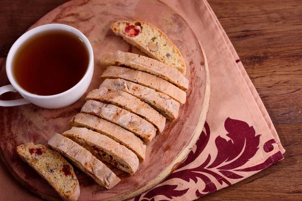 Delicious biscotti cookies with dried cherries and hazelnuts with black tea and white cup. Organic style. White cup of tea.