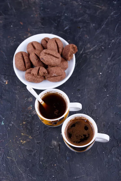 Delicious and fragrant coffee in the form of coffee, with grains of coffee, and small coffee cups on a black background