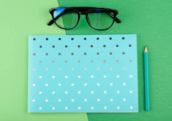 Синяя тетрадь с карандашом, очки, на зеленом фоне — стоковое фото