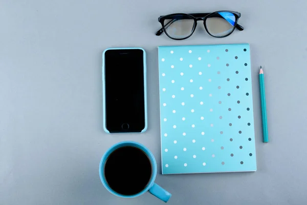Синяя тетрадь с голубым карандашом на сером фоне. Телефон, стаканы и чашка кофе . — стоковое фото