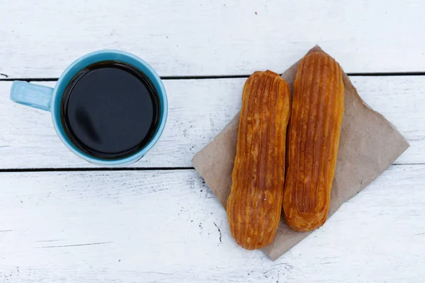 Café fragante en una taza azul con eclairs en la calle sobre una mesa de madera — Foto de Stock