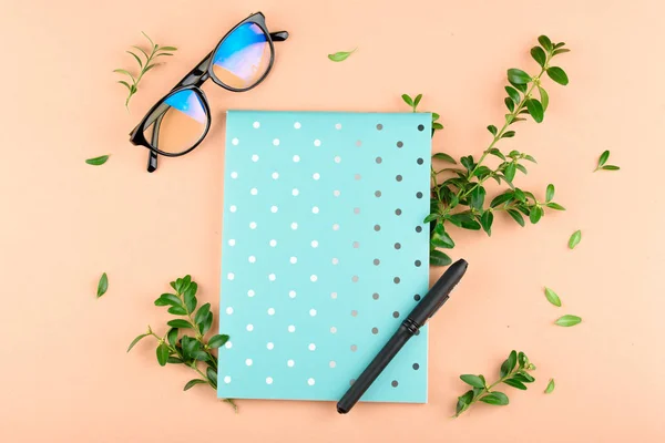 Blå anteckningsbok i en cirkel med en penna, glas, gröna blad, på en färgad bakgrund. — Stockfoto