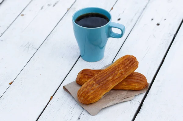 Café perfumado em uma xícara azul com eclairs na rua em uma mesa de madeira — Fotografia de Stock