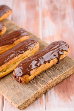 Ahşap bir tahta üzerinde çikolata ile lezzetli ve güzel eclairs. Iştah açıcı bir tatlı. Parti malzemeleri
