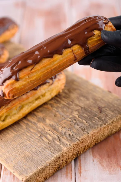 Sabrosas y hermosas eclairs con chocolate en una tabla de madera. Ap — Foto de Stock