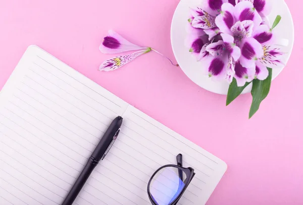 향기로운 아름다운 꽃, 분홍색 배경, 펜과 안경이있는 노트북. — 스톡 사진