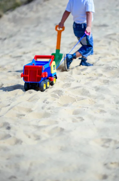 Menino na praia com um carro de brinquedo na areia — Fotografia de Stock