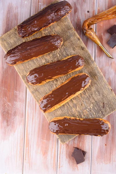 Sabrosas y hermosas eclairs con chocolate en una tabla de madera. Postres apetitosos. Artículos de fiesta — Foto de Stock