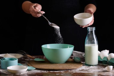 Cook'un elleri koyu bir arka plan üzerinde hamur için şeker dökün. Tatlı yapma süreci.