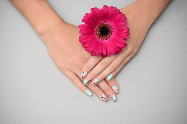 Vrouw hand met trendy Nail Art manicure Holding gerbera's bloem op grijze achtergrond — Stockfoto