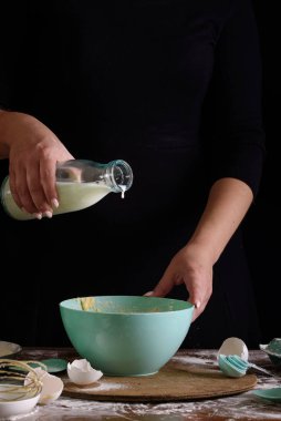 Koyu bir arka plan üzerinde aşçı eller hamur yoğurun. Tatlı yapma süreci. Süt.