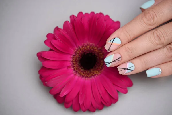 Kobieta ręka z modnym Nail Art manicure gospodarstwa gerbery kwiat na szarym tle — Zdjęcie stockowe