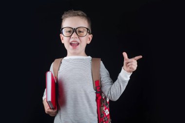 Siyah bir arka plan üzerinde neşeli gülümseyen küçük çocuk. Kameraya bakıyorum. Okul konsepti