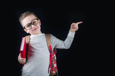 Siyah bir arka plan üzerinde neşeli gülümseyen küçük çocuk. Kameraya bakıyorum. Okul konsepti