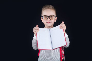 Siyah bir arka plan üzerinde neşeli gülümseyen küçük çocuk. Kameraya bakıyorum. Okul konsepti